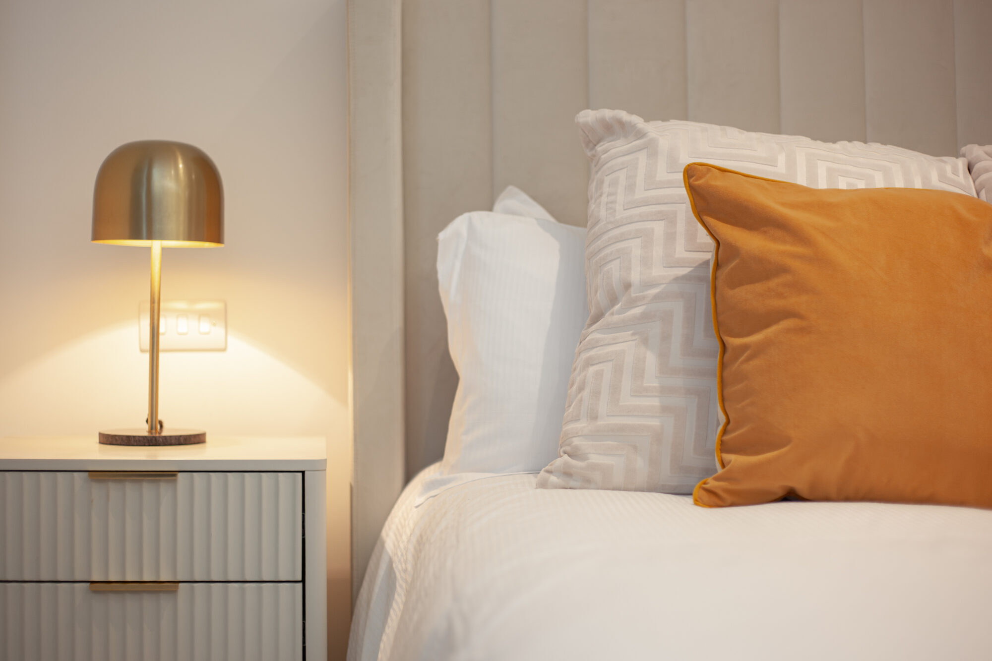 Comodino con lampada dorata e cuscino arancio
